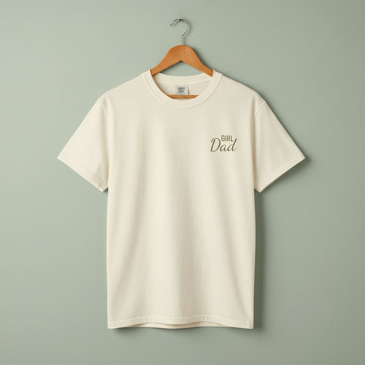 Beige t-shirt with 'Girl Dad' text on a hanger against a light green background