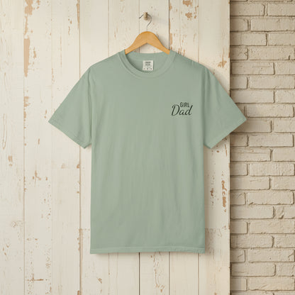 Mint green t-shirt with 'Girl Dad' text on a wooden hanger against a rustic brick wall.