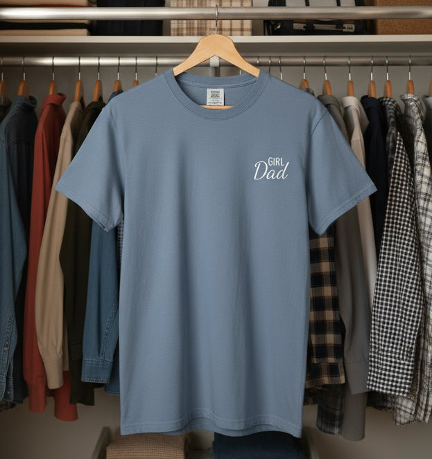 Blue t-shirt with 'Girl Dad' text on a hanger in a clothing store.
