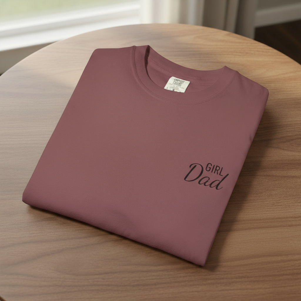 Folded maroon t-shirt with 'Girl Dad' text on a white background