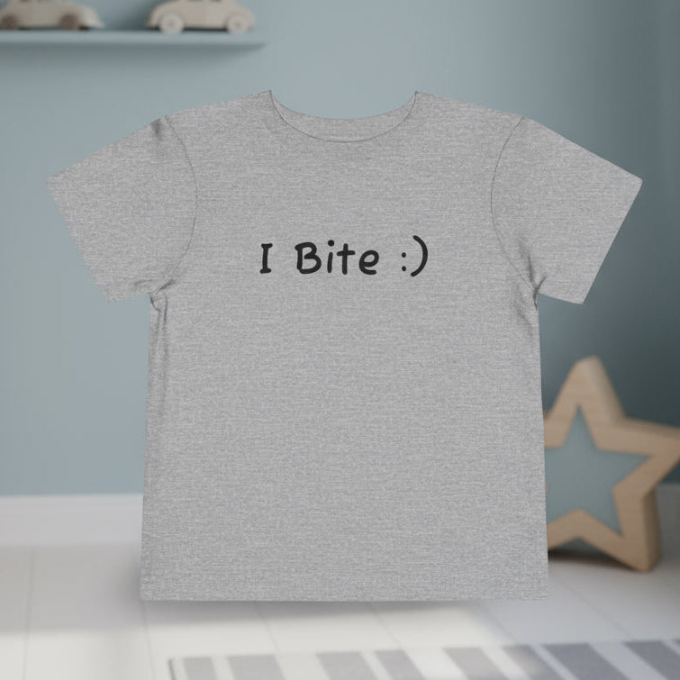 Gray t-shirt with 'I Bite :)' text in a child's room with toys and furniture.