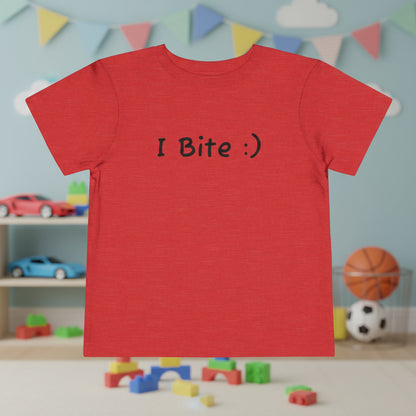 Red t-shirt with 'I Bite :)' text in a room with toys and colorful flags.